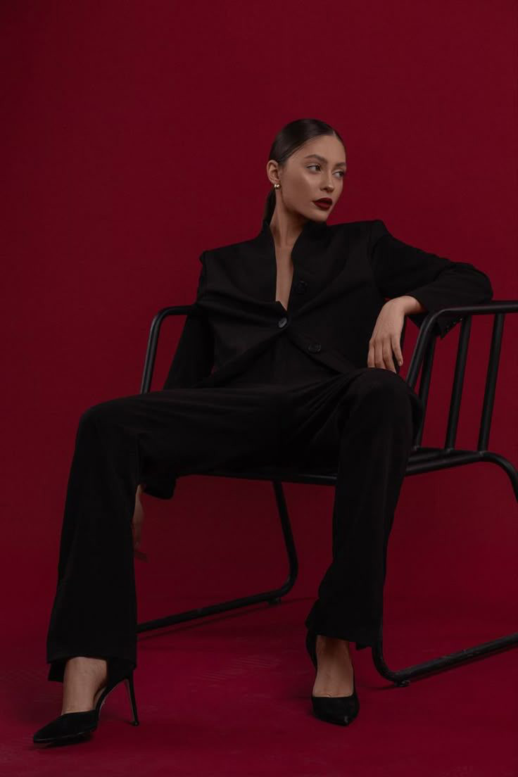 Woman in a tailored black suit against a deep red backdrop