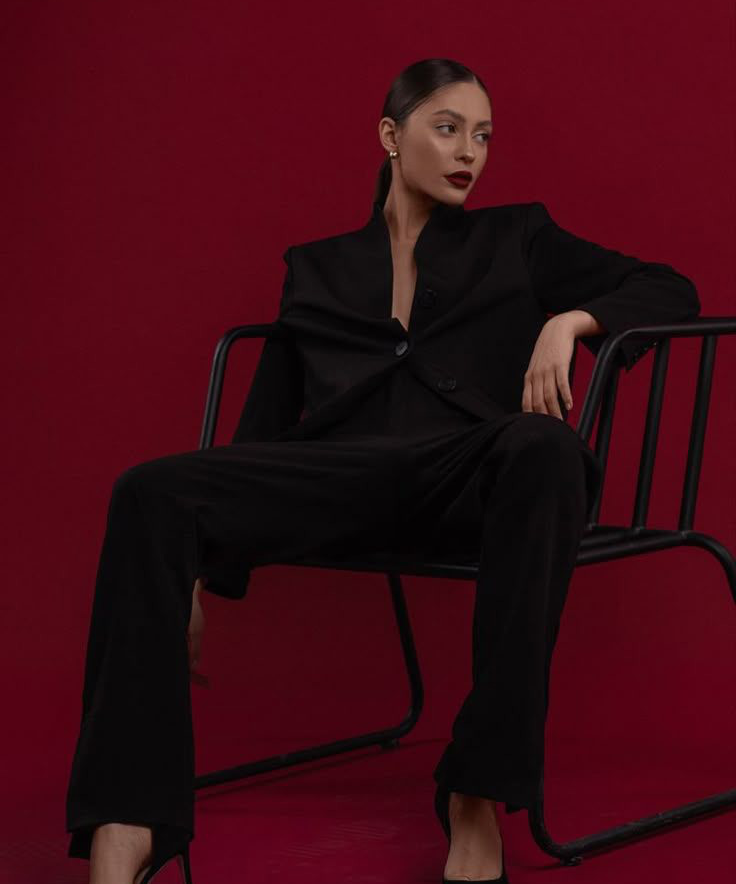 Woman in a tailored black suit against a deep red backdrop